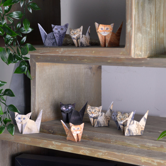 Lots of folded origami paper cats on a wooden shelf