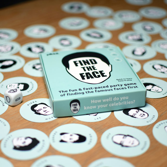 Find the face by Pikkii packaging on table with cards and dice scattered