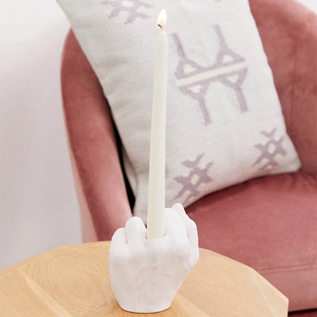 Pikkii Middle Finger Candle Holder with a lit candle on side table in front of a sofa chair