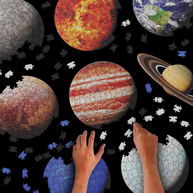 Hands assembling Pikkii Planets Jigsaw Puzzle over Black Background 