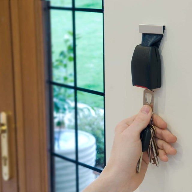 Hand holding keyring and keys plugging into Pikki Seatbelt Buckle Key Holder on wall near entrance