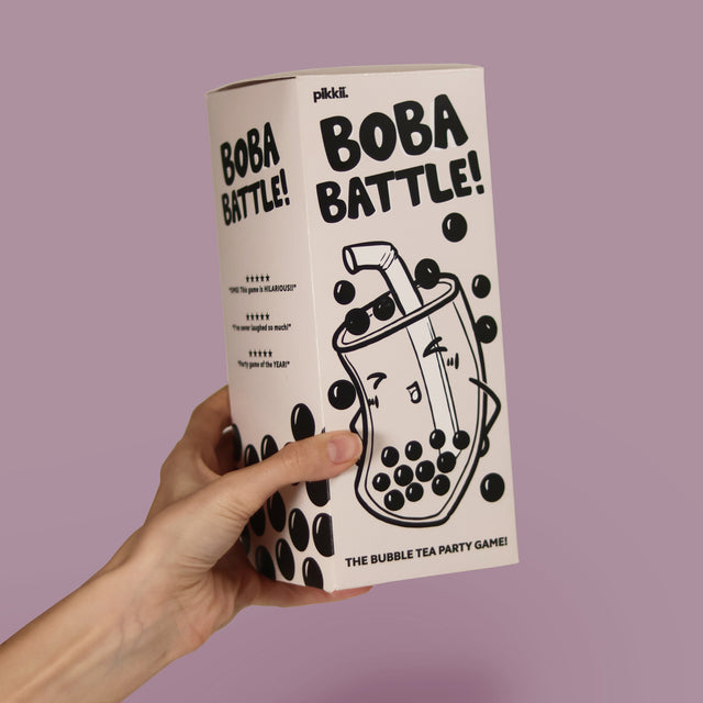 A hand holding the Boba Battle party game box by Pikkii, featuring playful bubble tea illustrations and customer reviews on a pastel purple background.