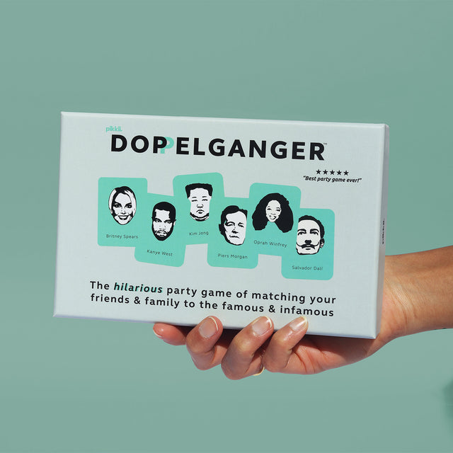 Hand holding Doppelganger party game packaging on green background