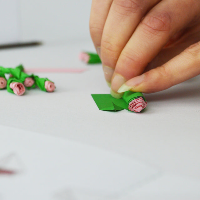 Hand rolling a little pink paper rose in a green paper leaf