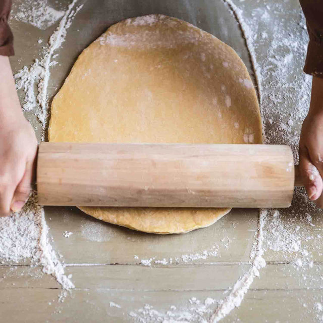 man using rolling pin to roll cookie dough on table covered in flour