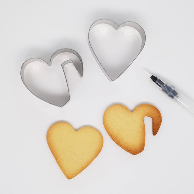 Two Heart Shaped Cookie Cutters two baked cookies and a food colouring pen on white background