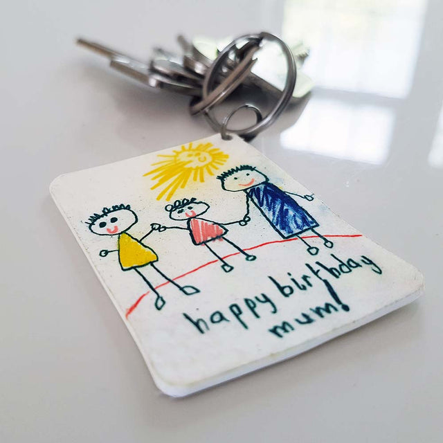 Close up of Piikkii Kids Drawing Shrink keyring with personalised Happy Birthday message attached to keys over white surfice