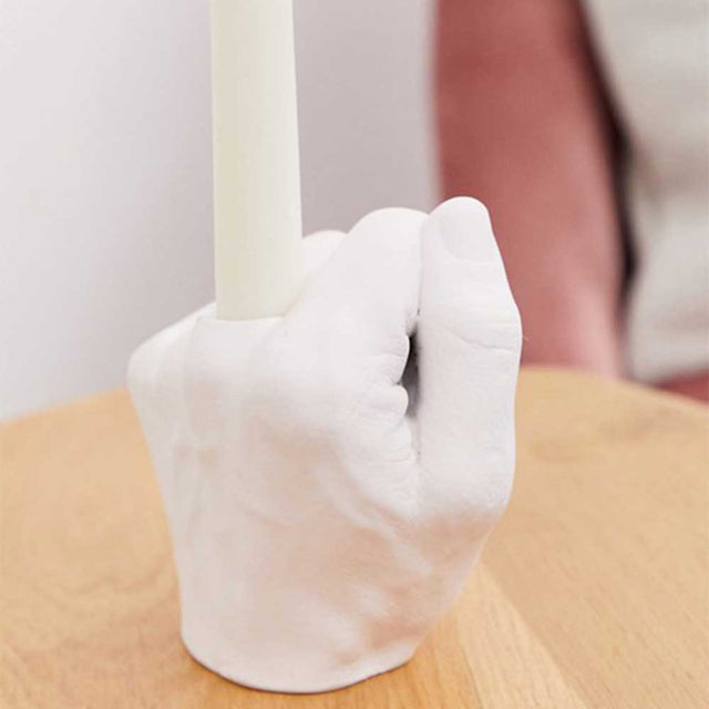 Close up of Pikkii Middle Finger Candle Holder with a candle on side table in front of a sofa chair