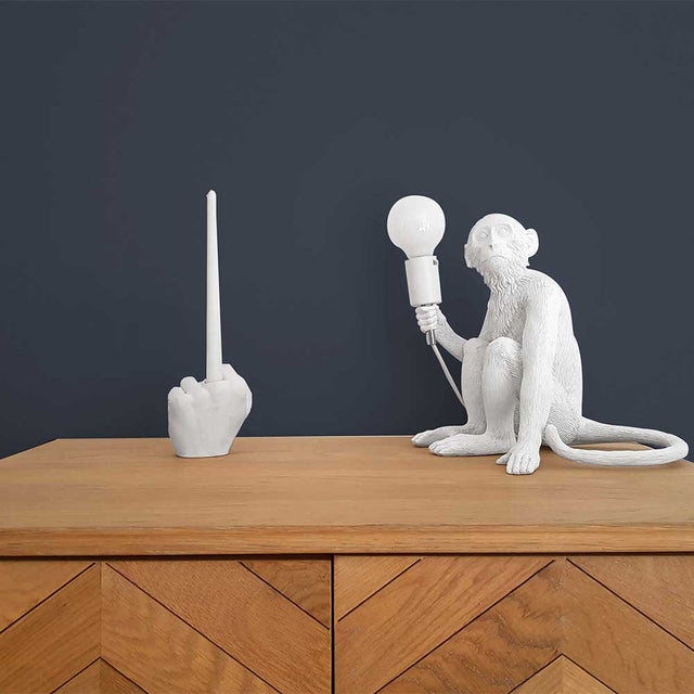 Pikkii Middle Finger Candle Holder on wooden surface next to monkey lamp 