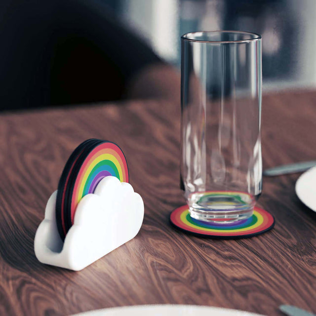 Nesting wooden rainbow colour coasters in a white ceramic cloud holder with a glass of water on a wooden dining table
