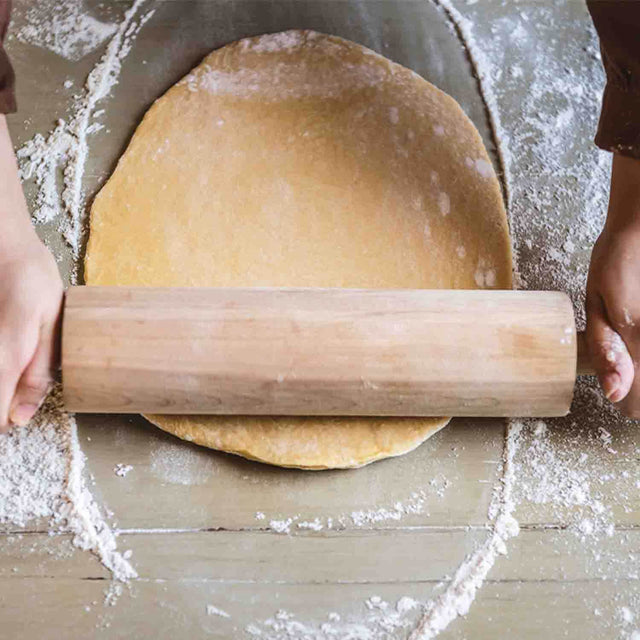 close up of man rolling cookie dough with large rolling pin